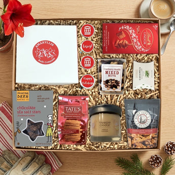Amaryllis gift set with a bulb kit, chocolates, cookies, pretzels and a candle beside a blooming amaryllis