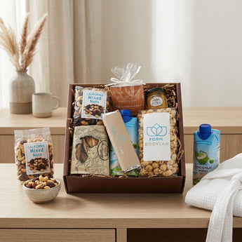 Large amenity snack box with California mixed nuts, Harney and Sons tea, honey mustard, coconut water, chocolate and caramel popcorn, on an oak console in a calm retreat room