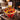 Autumn cupcake bouquet of red, orange, yellow and chocolate swirled cupcakes with chocolate maple leaves and a Happy Thanksgiving topper on a wooden pick, styled on a wood table by a fireplace