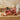 Autumn Harvest Gift Basket Regular size: a kraft gift box printed with red apples and tied with red gingham ribbon, filled with fall treats, with a matching closed apple print box beside it, styled on a light oak console table against a warm beige wall
