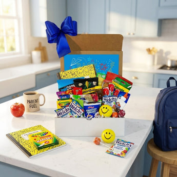 Back to school snack box with a royal blue bow, packed with Welch's fruit snacks, Smartfood popcorn, Frosted Flakes, Crayola crayons and school supplies, on a kitchen island with a composition notebook, smiley stress ball and a kids backpack