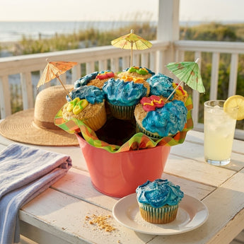 Beach cupcake bouquet with blue wave and graham crumb sand cupcakes, fondant flip flops and crabs and paper cocktail umbrellas in a coral pail, styled on a beach house porch table