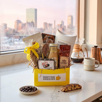 Boston Brewins coffee gift box with biscotti, coffee and espresso beans on a counter with a Boston skyline sunrise