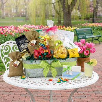 Boston Public Garden gift basket, a galvanized tub tied with a green polka dot ribbon, filled with pretzels, mixed nuts, chocolates, cookies and swan note cards, on a cafe table by spring tulips