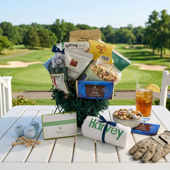 Boston Tee-Par-Tee Golf Gift Basket, golf snacks, coffee, chocolate and an embroidered golf towel, on a clubhouse patio table overlooking the fairway