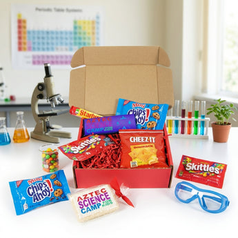 Small camp snack box in red with a sample camp logo, filled with Chips Ahoy, Skittles, Cheez-It and Starburst, on a science lab table with a microscope and safety goggles