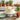 Carrot cake with cream cheese frosting and piped carrot decorations on a white pedestal stand, styled on a weathered potting bench with terracotta pots, fresh carrots and chopped walnuts