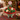 Christmas Basket Cupcake Bouquet of 19 cupcakes domed in a wicker basket, red, green and white buttercream swirls with holiday sprinkles, Christmas tree cupcakes and a pretzel antler reindeer, a red ruffle, green gingham bow and Merry Christmas topper, in front of a lit Christmas tree