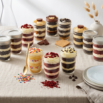 Twelve assorted layered cupcake jars in mixed flavors arranged on a wooden party table