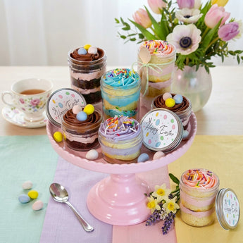 Easter Cupcake Jars, layered cupcake jars with pastel frosting and candy egg nests on a pink cake stand, on an Easter brunch table