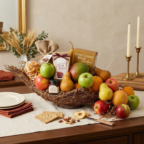 Fall Harvest Cornucopia gift basket with fresh apples, pears, oranges, stone ground wheat crackers, bog bites, mixed nuts and preserves, styled on a linen draped walnut sideboard with brass candlesticks