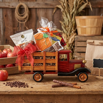 Wooden farm truck gift loaded with Boston's Best coffee, Ghirardelli chocolate, cocoa and a hand painted pumpkin sugar cookie, styled on a farm stand counter with apple crates and corn stalks