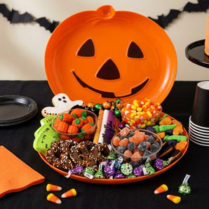 Halloween sweets grazing board on a jack o lantern platter with gummies, candy corn and chocolate pretzels