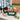 Holiday Crunch Gift Box Large size: a dark green gift box with a cream Holiday Crunch label and a matching closed green box with a red bow beside it, filled with holiday snacks and treats, styled on a white quartz office kitchen counter with tall windows onto a snowy city