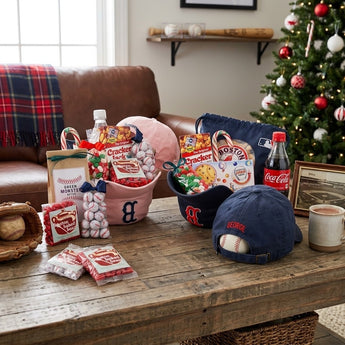 Holiday Play Ball gift in a navy Red Sox cap filled with ballpark snacks and candy on a den coffee table by the Christmas tree