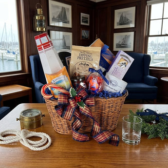 Holiday Sails wicker gift basket with tartan plaid bow, lighthouse box, dipping pretzels and nuts on a teak table in a yacht club lounge