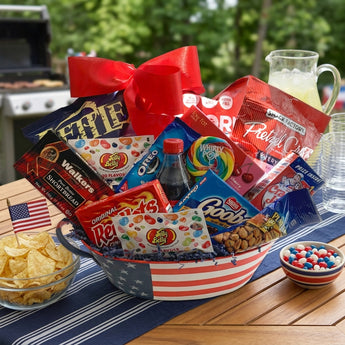 July 4th Snack Basket, an American flag basket of Jelly Belly, Walkers shortbread and snacks with a red bow, on a patio table at a Fourth of July party