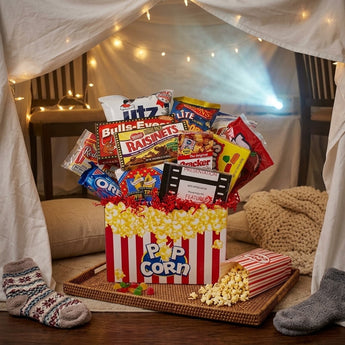Popcorn box movie night gift packed with candy and snacks inside a cozy living room blanket fort