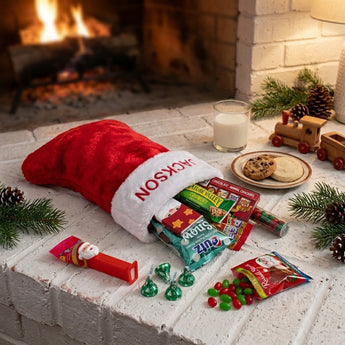 Personalized red plush Christmas stocking with name cuff filled with holiday treats on a fireplace hearth