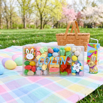 Personalized Easter Tackle Box of Candy, a clear tackle box of pastel Easter candy with a personalized name, on a picnic blanket after an egg hunt