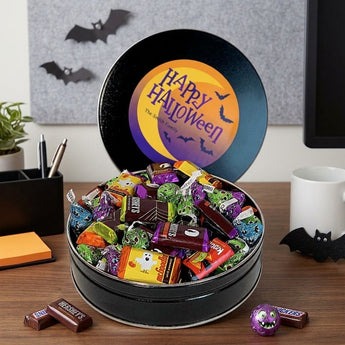 Personalized Halloween candy tin with a printed Happy Halloween lid, heaped with wrapped candy on an office desk