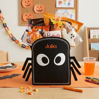 Personalized trick or treat bag in black felt spider design filled with Halloween candy on a classroom party table