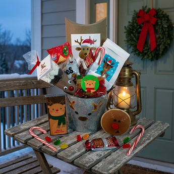 Galvanized reindeer gift bucket filled with holiday treats on a snowy front porch table