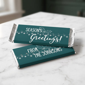 Season's Greetings personalized candy bars in teal wrappers with a family name on a marble counter