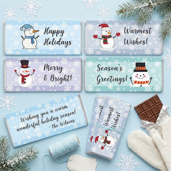 Overhead flat lay of snowman personalized chocolate bars with holiday greetings on a pale blue table