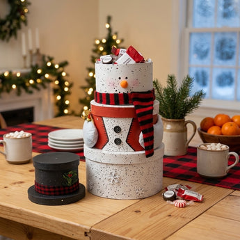 Snowman Tower gift boxes, four stacked round boxes with a buffalo check scarf and black top hat lid, styled on a pine farmhouse table with cocoa mugs and a buffalo check runner