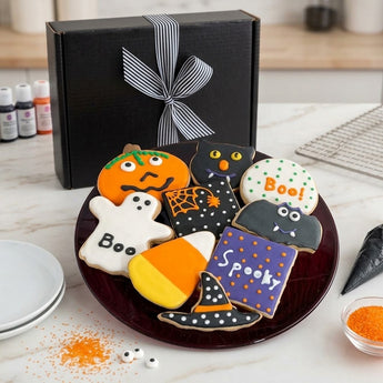 Spooky frosted Halloween cookies on a burgundy plate with a black ribbon tied gift box on a bakery counter