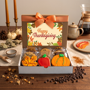 Thanksgiving cookies and brownies gift box with hand iced pumpkin, acorn and autumn leaf cookies, styled on a walnut table with candlesticks, a coffee pot and small white pumpkins