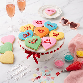 Valentine's Day Conversation Heart Sugar Cookies, iced heart cookies with sweet messages on a white cake stand with pink lemonade and sprinkles