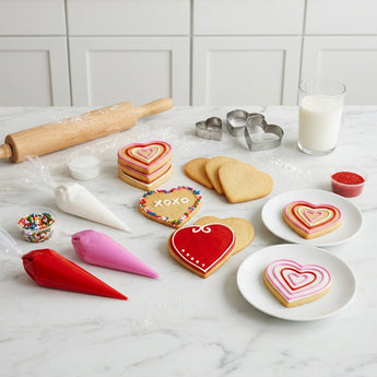 Valentine's Day Cookie Decorating Kit, heart sugar cookies with red, white and pink icing bags and sprinkles, on a marble kitchen island with cookie cutters