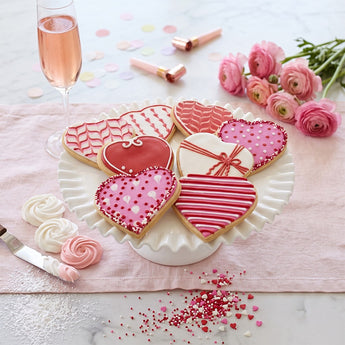Valentine's Day Iced Sugar Cookies, pink, red and white decorated heart cookies on a scalloped plate with roses and sparkling drinks
