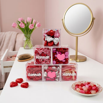 Valentine's Day Personalized Candy Pyramid, six clear cubes of red and pink candy personalized with a name, on a white bedroom vanity with pink tulips
