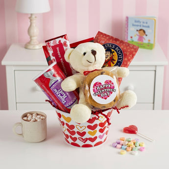 Valentine's Day Sweets Gift Basket, a heart basket with a cream teddy bear, a Happy Valentine's Day cookie, hot cocoa and Pirate's Booty, on a child's dresser