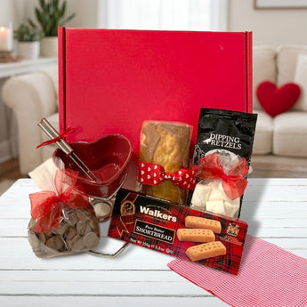 Valentine's Day fondue gift box with a heart-shaped red fondue pot, chocolate wafers, pound cake, dipping pretzels, marshmallows and Walkers shortbread, on a cozy Valentine's living room table