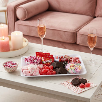 Valentine's Day Grazing Box, a candy board of Skittles, M&M's, Oreos, gummy hearts and conversation hearts, on a coffee table for a Galentine's night in