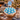 Winter Cupcake Bouquet of 19 cupcakes domed in a round wicker basket, sky blue buttercream with white chocolate snowflakes and a Happy Holidays topper, on a wooden table by a Christmas tree with hot cocoa