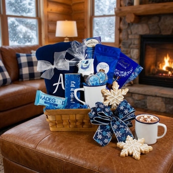 Winter snuggles gift basket with monogrammed fleece blanket, cocoa and treats on a cabin ottoman by the fire