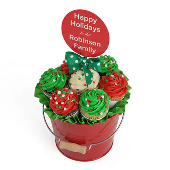 Red bucket filled with Christmas-themed cupcakes and a personalized 'Happy Holidays' sign.