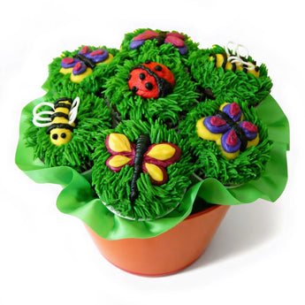 Decorative spring cupcake arrangement in a pot shaped container. The cupcakes have green frosting for grass and colorful nature inspired decorations such as butterflies, bees, and ladybug on them over a white background.