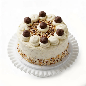 Decorative cake with white frosting, chocolate balls, and coconut flakes on a white stand.