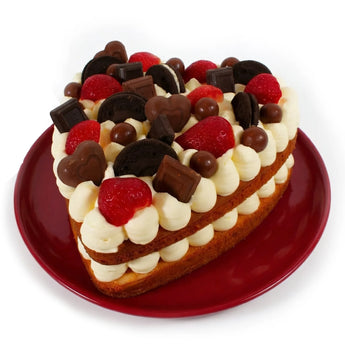 Heart-shaped cake with white frosting, red strawberries, and chocolate pieces on a red plate.