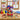 Crayon candy vase wrapped in crayons with a red ribbon, filled with Tootsie Pops, a rainbow swirl lollipop, Mike and Ike and jelly beans, on an art room table with paint jars and children's paintings