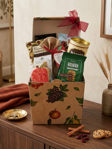 Harvest Treats fall gift box with cranberry harvest medley, Marich chocolates, Tate's cookies, an apple sugar cookie and cinnamon apple tea, styled on a walnut entry console with a rust scarf and a pear