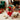 Nutcracker Sweet Holiday Gift Basket Regular size: a white gift box tied with a red bow, filled with holiday treats including a nutcracker tin, Nutcracker Sweets, Holly-Day Beans, chocolate truffles and shortbread, styled on a cream knit rug in front of a lit brick fireplace with stockings on the mantel