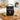 Black Igloo insulated lunch bag embroidered with a white letter T, on a butcher block kitchen counter with a sandwich, green apple, water bottle and pretzels