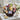 Thinking of You Gift Basket Medium size: a dark brown wicker basket with navy crinkle, filled with comfort treats including Cranberry Health Mix, daisy cookies, Hero preserves, Tasch flatbread and chocolate covered nuts, styled on a whitewashed wooden table by a sunny window with white hydrangeas
